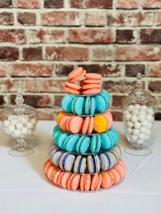 Six-tier macaron tower filled with macarons in coral, turquoise, blue, yellow and lilac, standing between two glass apothecary jars of white candy.