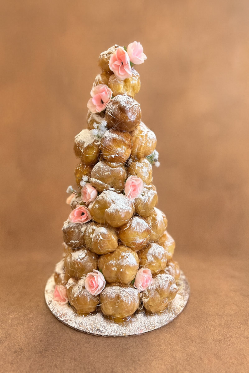 Croquembouche: a cone of caramel-glazed choux puffs dusted with icing sugar, wrapped in threads of spun caramel and dressed with pink sugar roses and small white blossoms.