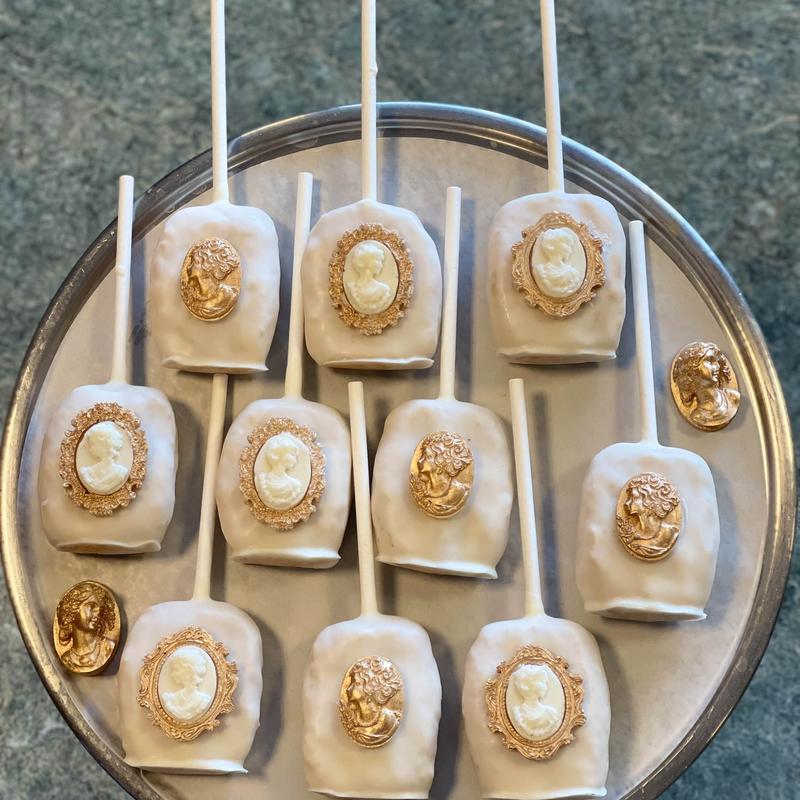 White-glazed cake pops seen from above on a silver tray, each set with a gold-framed ivory cameo medallion.