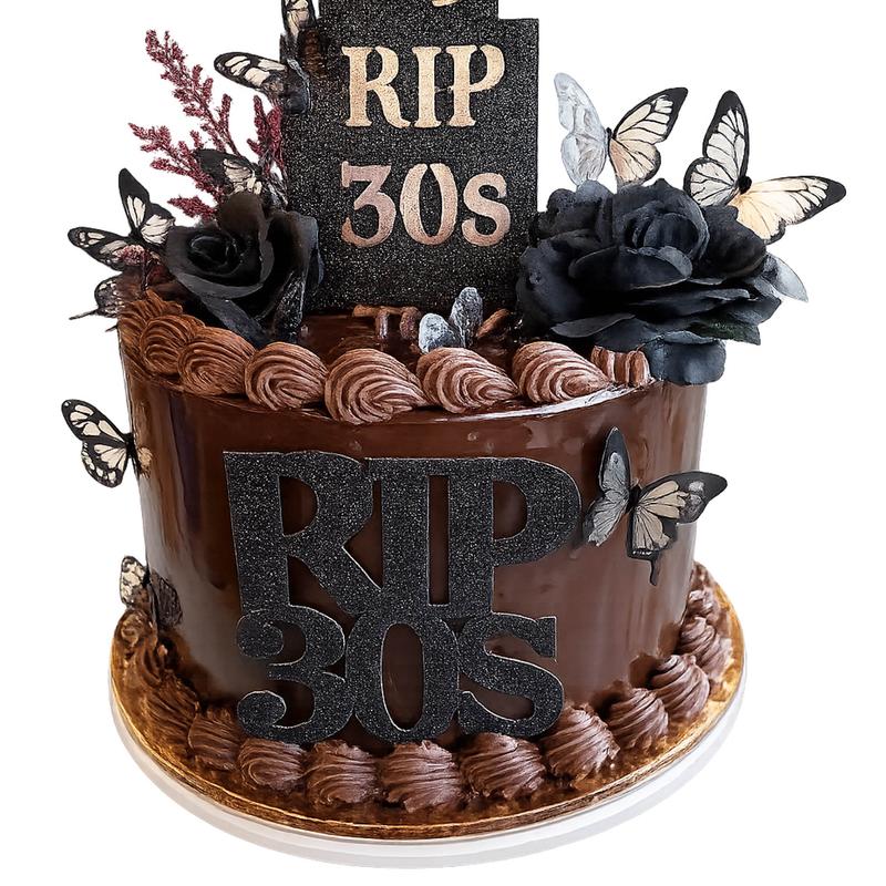 Chocolate ganache cake with piped chocolate shell borders, a black glitter RIP 30s plaque on the side and a matching headstone topper, dressed with black roses and cream-and-black paper butterflies.
