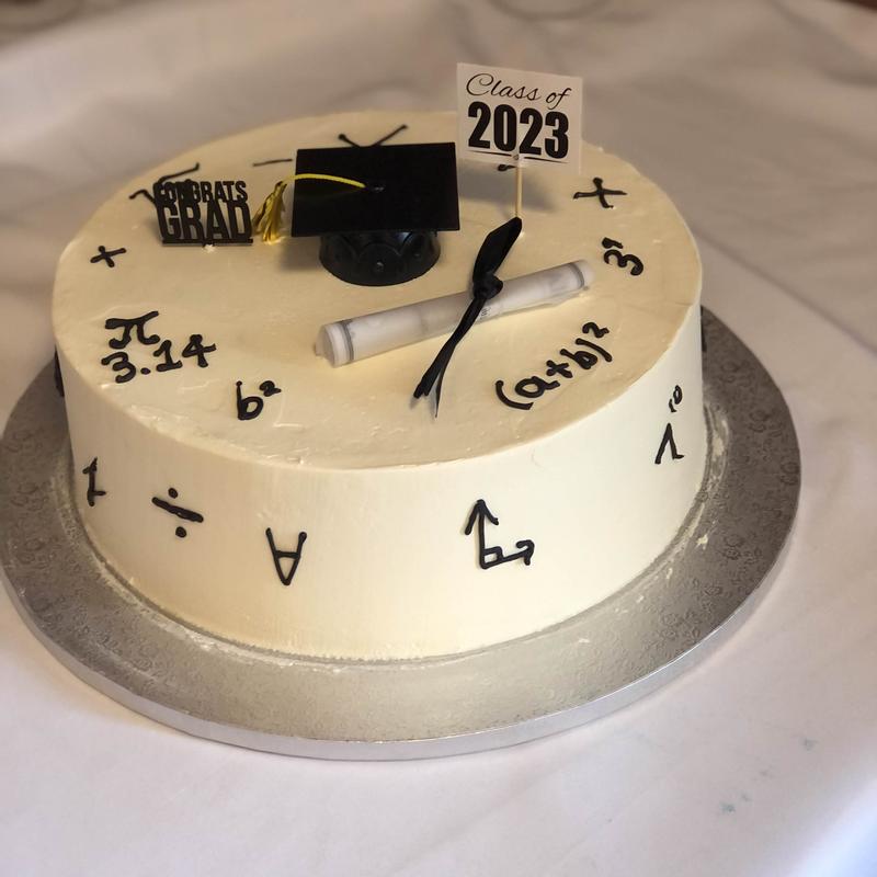 Ivory buttercream graduation cake hand-piped with black mathematical symbols and equations, topped with a fondant mortarboard, a rolled diploma and a Class of 2023 sign.