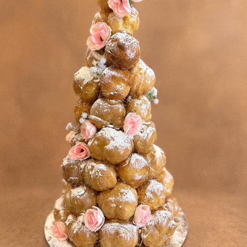 Croquembouche of glazed choux puffs dusted with icing sugar, wrapped in spun caramel and dressed with pink sugar roses and small white blossoms.