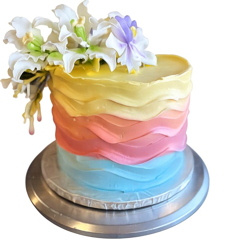 Cake wrapped in horizontal ruffled bands graded from blue through pink and coral to yellow, topped with a spray of white and lilac sugar lilies.
