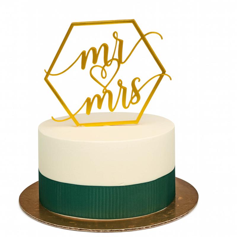 Single-tier wedding cake in smooth ivory over a combed forest-green band, topped with a gold hexagon mr and mrs cutout, on a gold cake board.