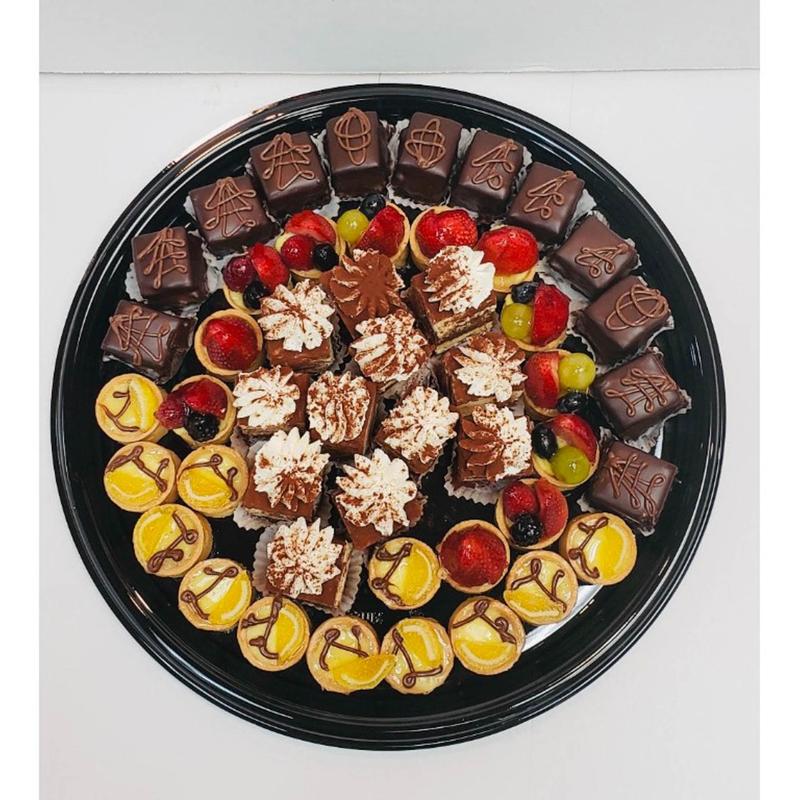 Large round dessert platter arranged in rings of chocolate-glazed petits fours, cocoa-dusted tiramisu squares, citrus tartlettes and fruit tartlettes topped with berries.