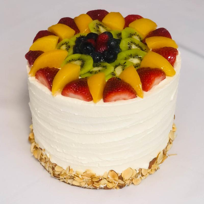 Round cake in ridged white cream with toasted almond flakes pressed around the base, topped with a sunburst of strawberries, peach slices and kiwi around a centre cluster of berries.