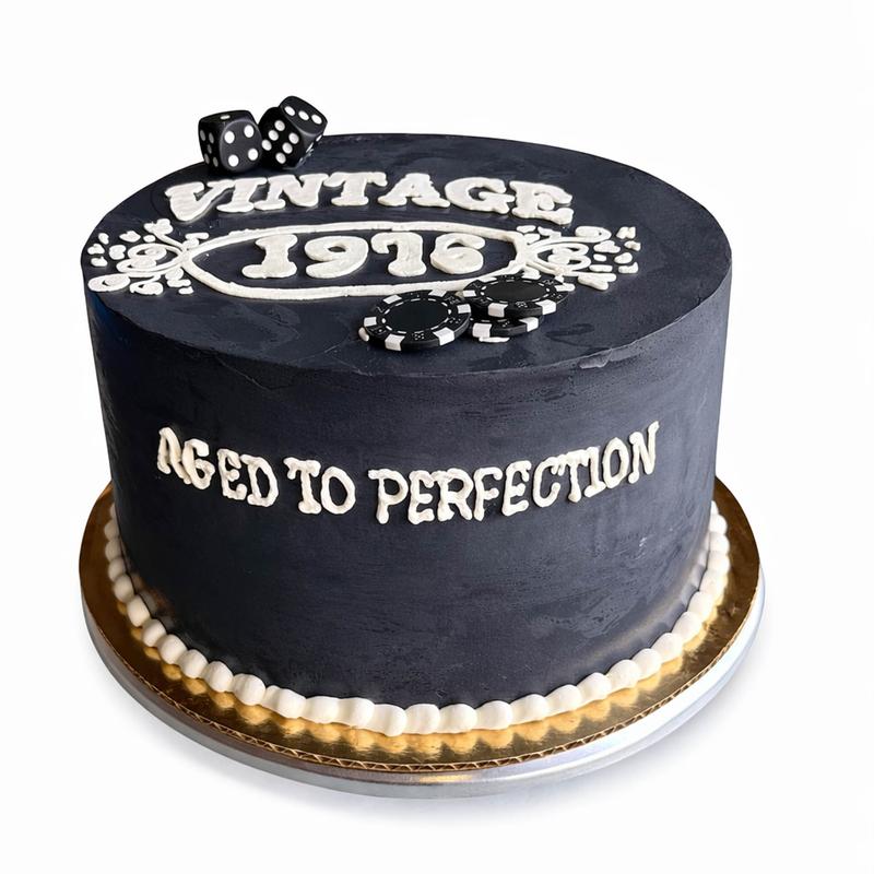 Charcoal buttercream cake lettered Vintage 1976 and Aged to Perfection in white icing, decorated with black dice and poker chips over a white pearl border.
