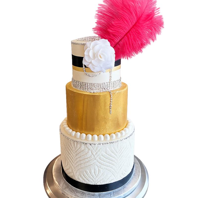 Art-deco three-tier cake: an embossed white base tier, a burnished gold middle tier and a black-and-ivory top tier, banded with rhinestone trim and finished with a white sugar rose and a tall pink feather.