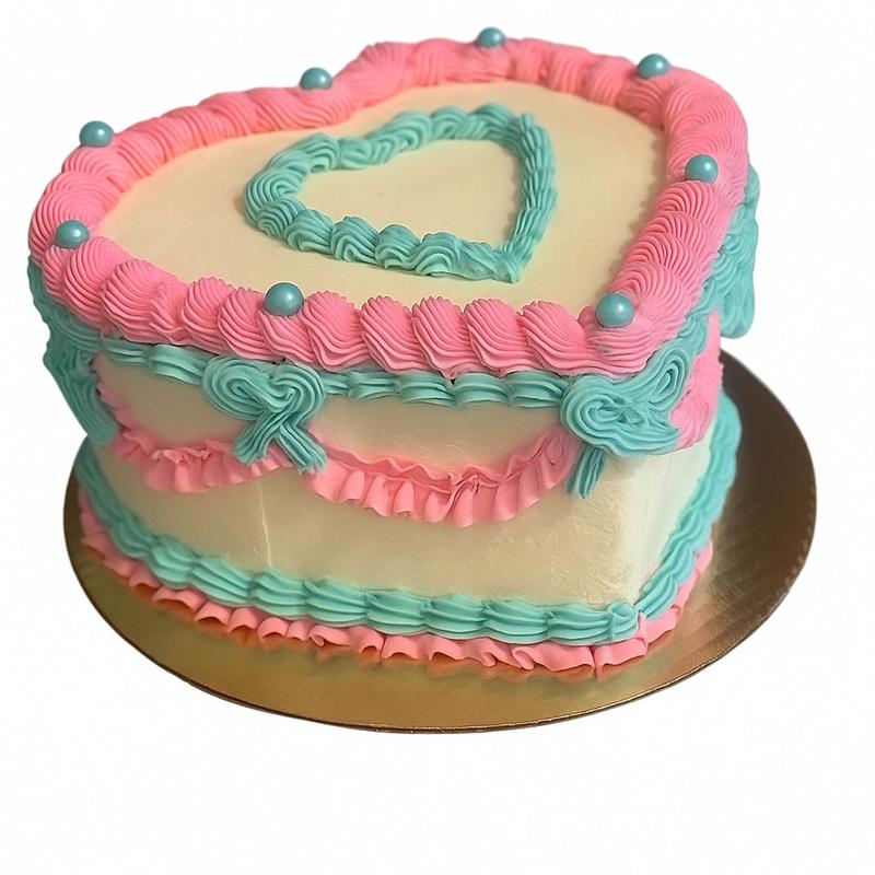 Heart-shaped cake in ivory buttercream with vintage piping: pink ruffled borders, turquoise rosettes and bows, sugar pearls and a piped turquoise heart on top.