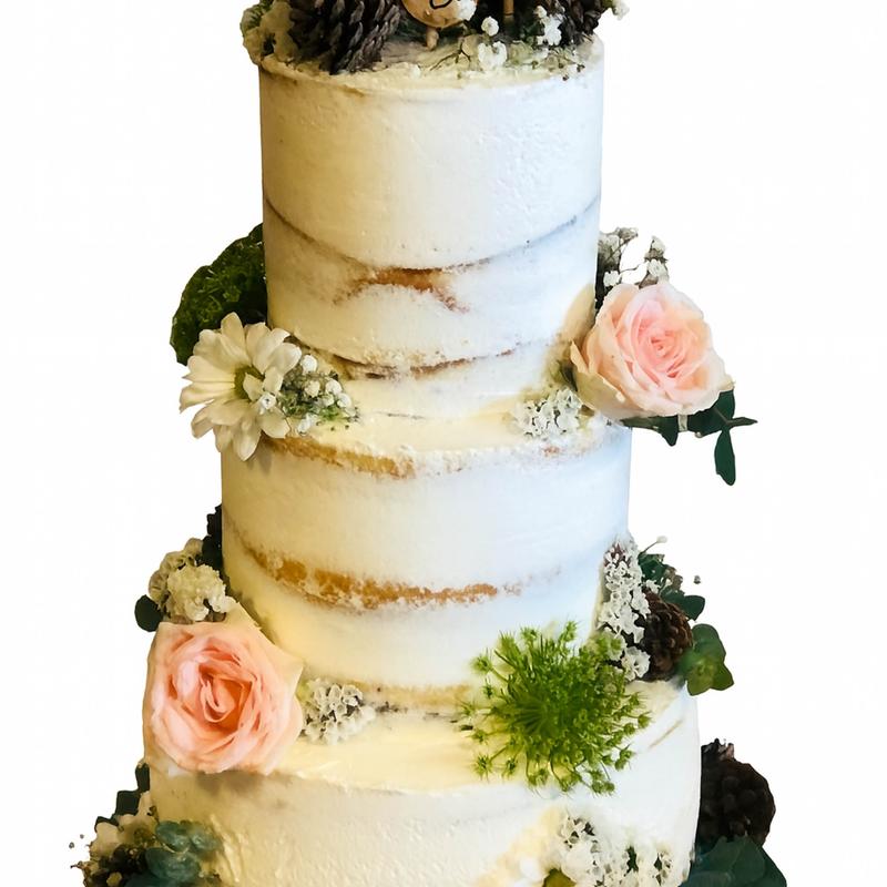 Three-tier semi-naked wedding cake with the sponge showing through a thin white coat, dressed with blush roses, white daisies, baby's breath, pinecones and moss.