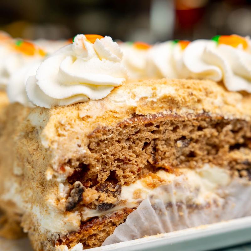 Close-up of a carrot cake slice showing spiced sponge layered with cream and coated in cake crumb, finished with a piped cream rosette.