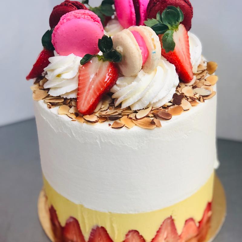 Fraisier cake: a band of halved strawberries set in yellow cream around the base, a white cream collar above, and a crown of toasted almond flakes, piped cream, strawberries and macarons.