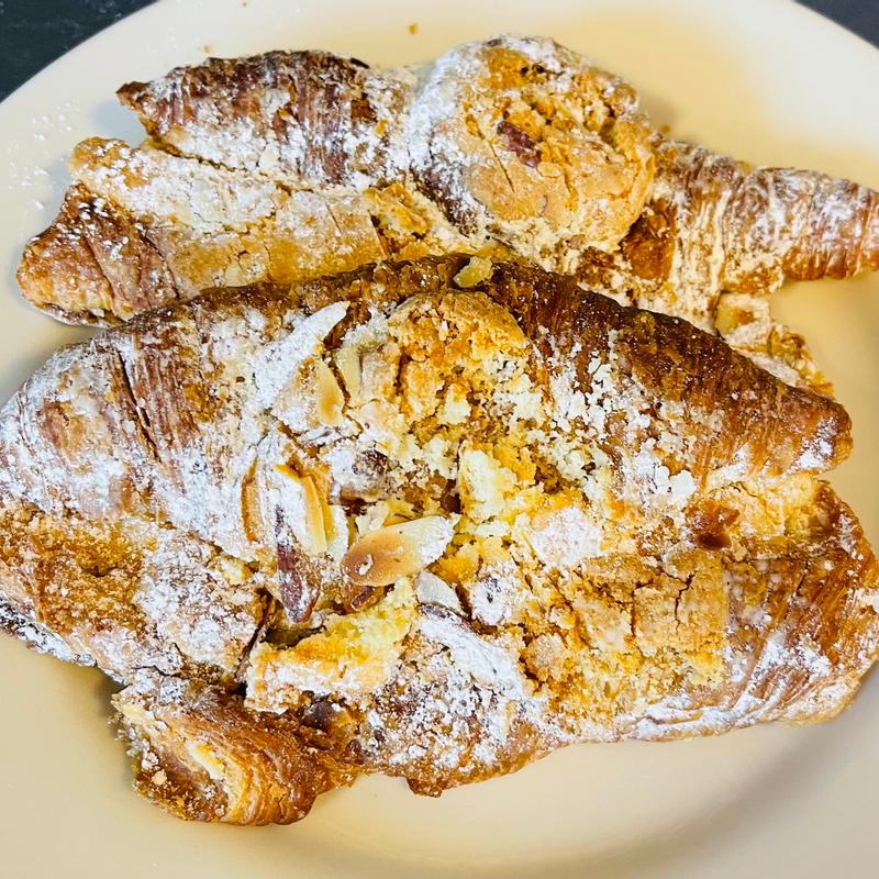 Almond croissants on a plate, split and filled with almond cream, scattered with flaked almonds and dusted heavily with icing sugar.