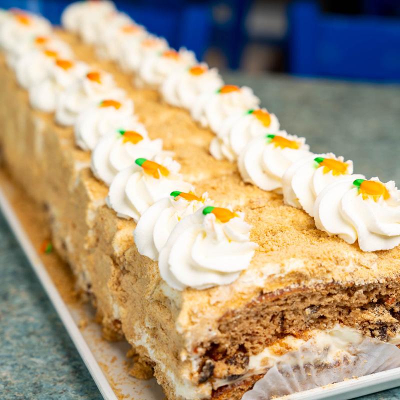 Long carrot loaf cake coated in cake crumb, lined the full length with piped cream rosettes each finished with a tiny orange carrot.