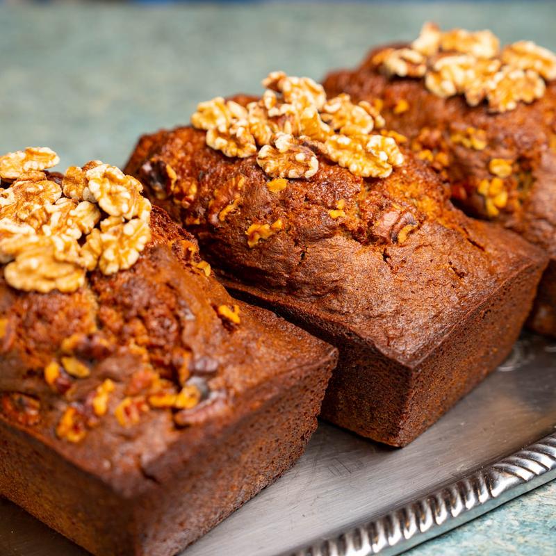 Row of small dark loaf cakes on a silver tray, each crowned with whole walnut halves.
