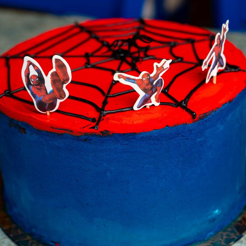 Round cake in blue buttercream with a red top piped with a black spider web, topped with three Spider-Man figure picks.