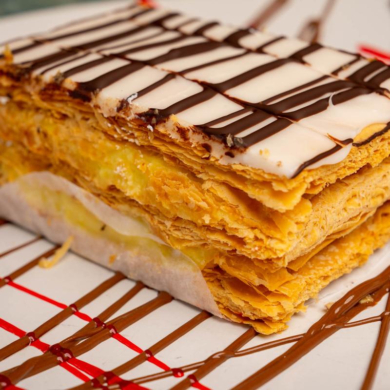 Slice of mille-feuille, its layers of caramelised puff pastry and pastry cream stacked high under a white fondant top marbled with dark chocolate.