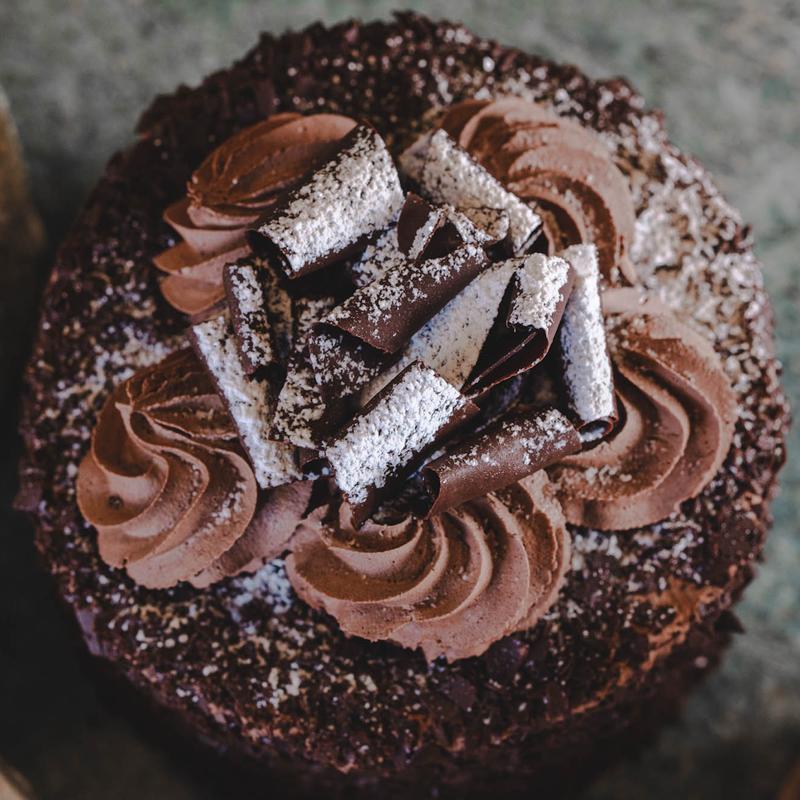 Chocolate cake seen from above: chocolate crumb around the rim, a ring of piped chocolate cream rosettes and a pile of chocolate curls dusted with icing sugar at the centre.