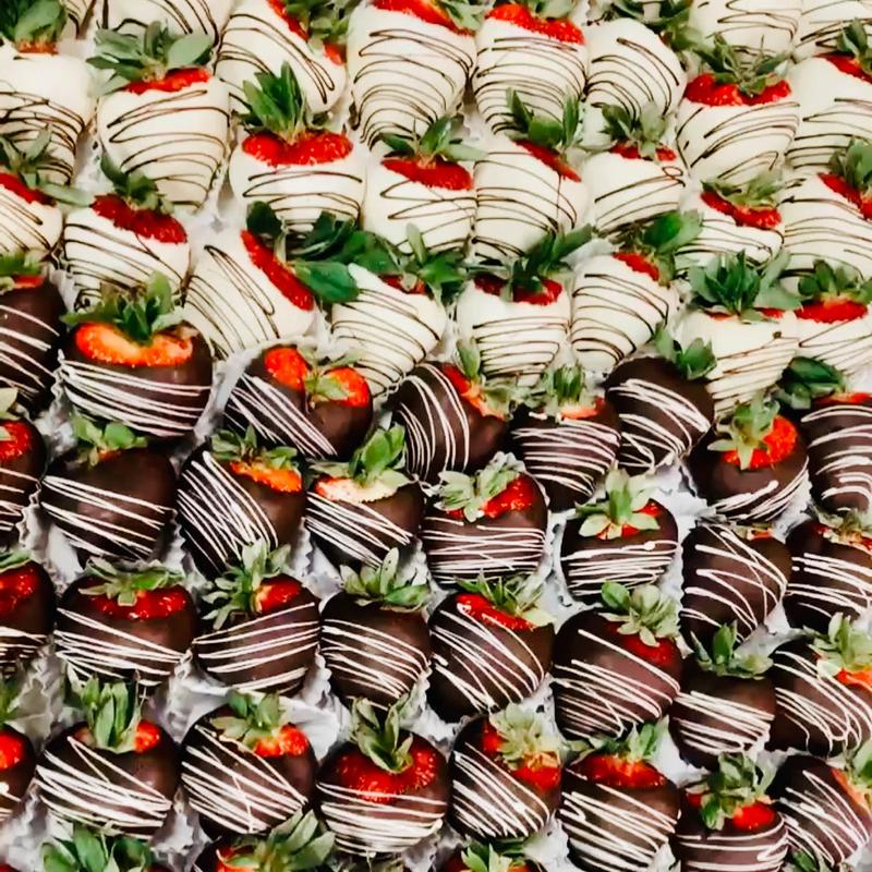Rows of chocolate-dipped strawberries, the front rows in dark chocolate striped with white and the rows behind in white chocolate striped with dark.