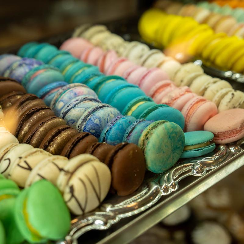 Silver display trays crowded with macarons in rows of chocolate, marbled blue, turquoise, pink, cream, green and yellow.