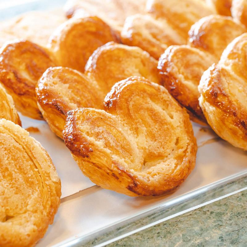 Close-up of golden palmiers on a metal tray, their caramelised sugar layers curled into hearts.