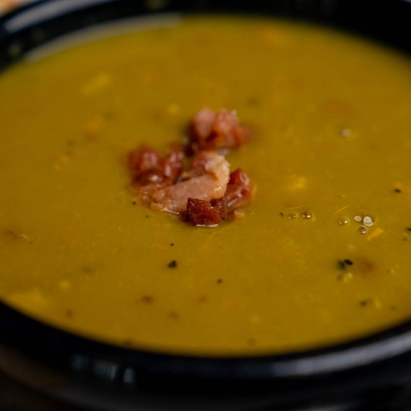 Close-up of a bowl of thick split pea soup topped with chopped bacon and cracked pepper.