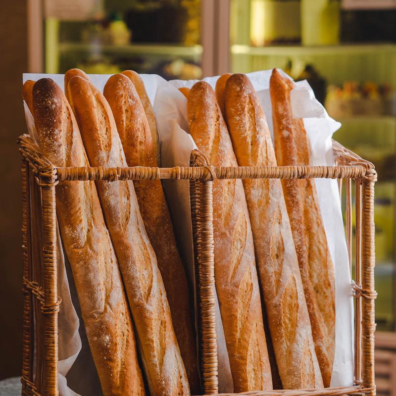 Wicker basket lined with paper and filled with upright baguettes, the bakery cases glowing behind.