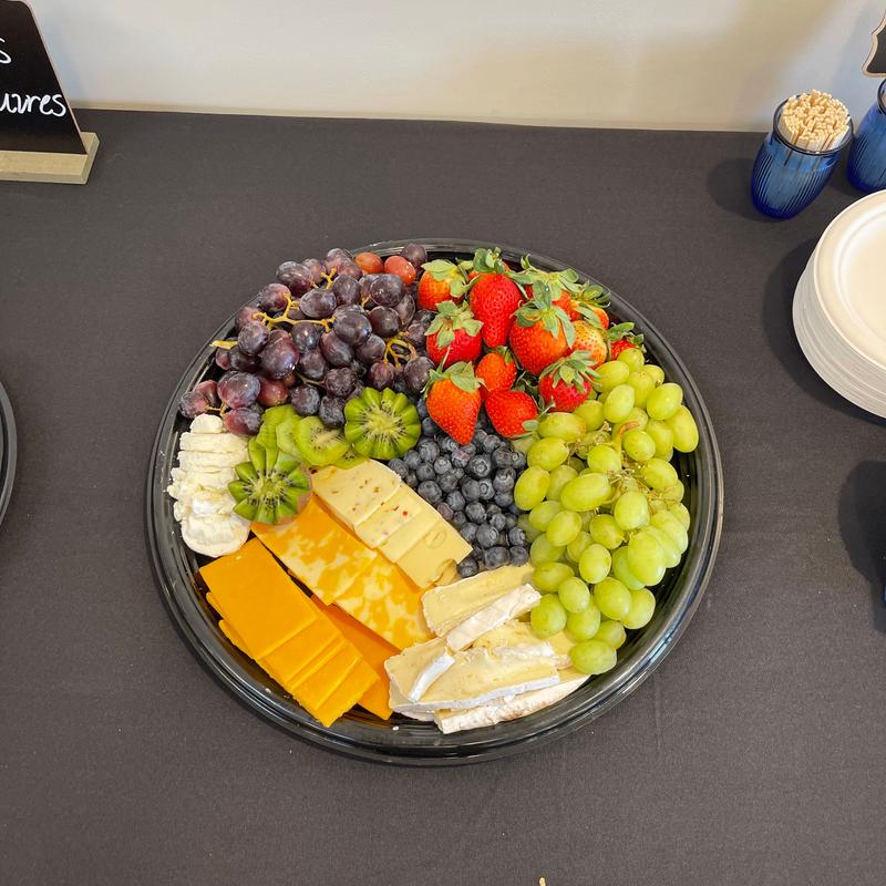Round catering platter seen from above, arranged in wedges of cheddar, pepper jack and brie with kiwi, red and green grapes, blueberries and strawberries.