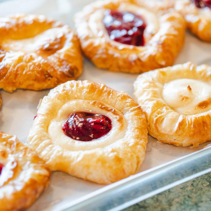 Tray of glazed danish pastries, some filled with red jam and others with vanilla custard.