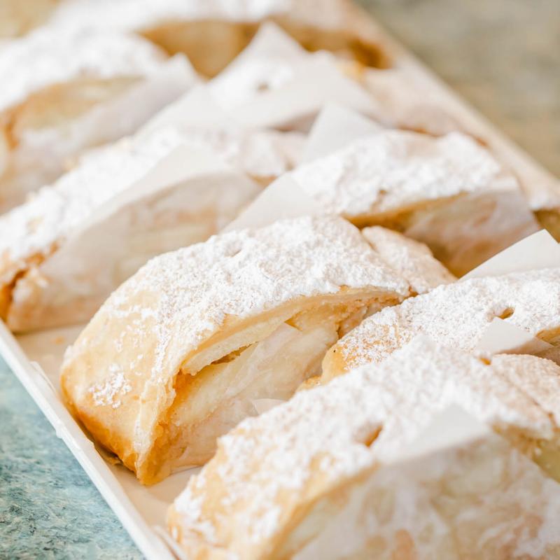 Row of golden turnovers filled with sliced apple and dusted heavily with icing sugar.
