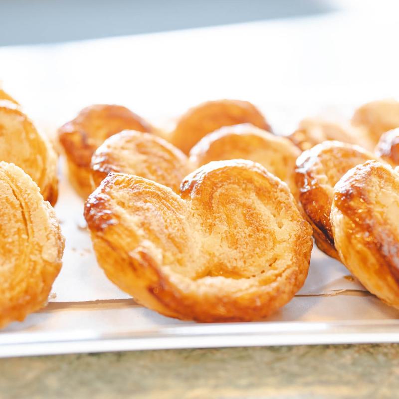 Row of golden caramelised palmiers on parchment, their sugared layers curled into hearts.