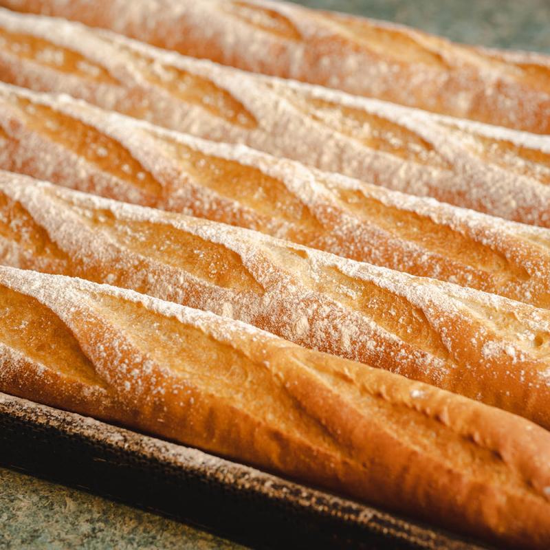 Baguettes fresh from the oven on a baking tray, slashed tops dusted with flour.