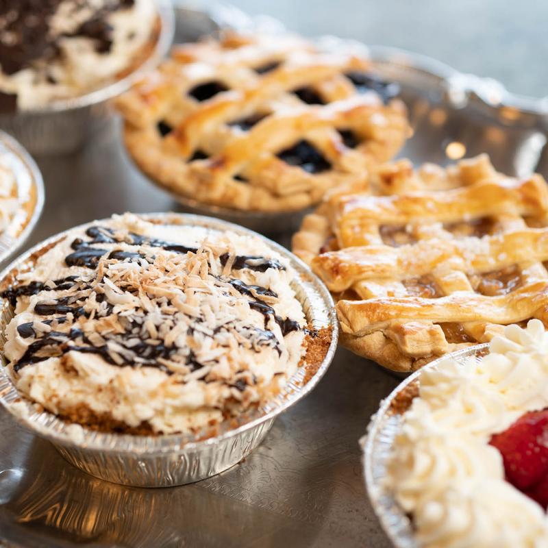 Individual pies on a silver tray: a coconut cream pie drizzled with chocolate, a lattice blueberry pie, a lattice apple pie and a cream-topped strawberry pie.