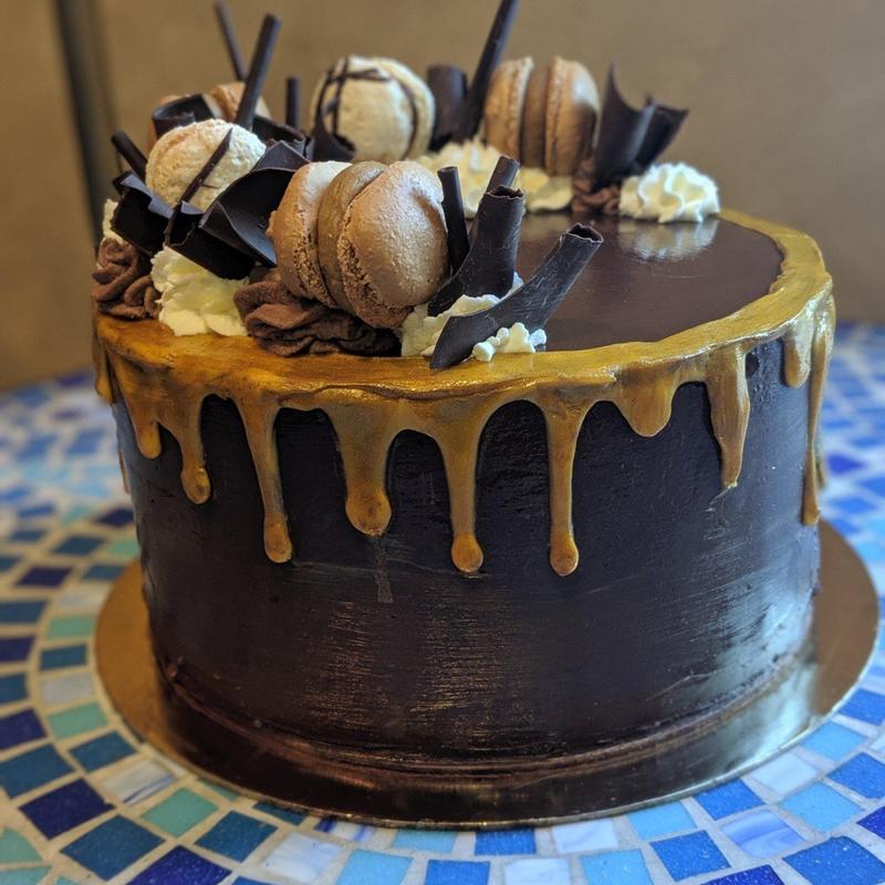 Gold drip chocolate cake: dark chocolate ganache with a gold drip running down the sides, crowned with chocolate macarons, chocolate shards, piped chocolate rosettes and cream.