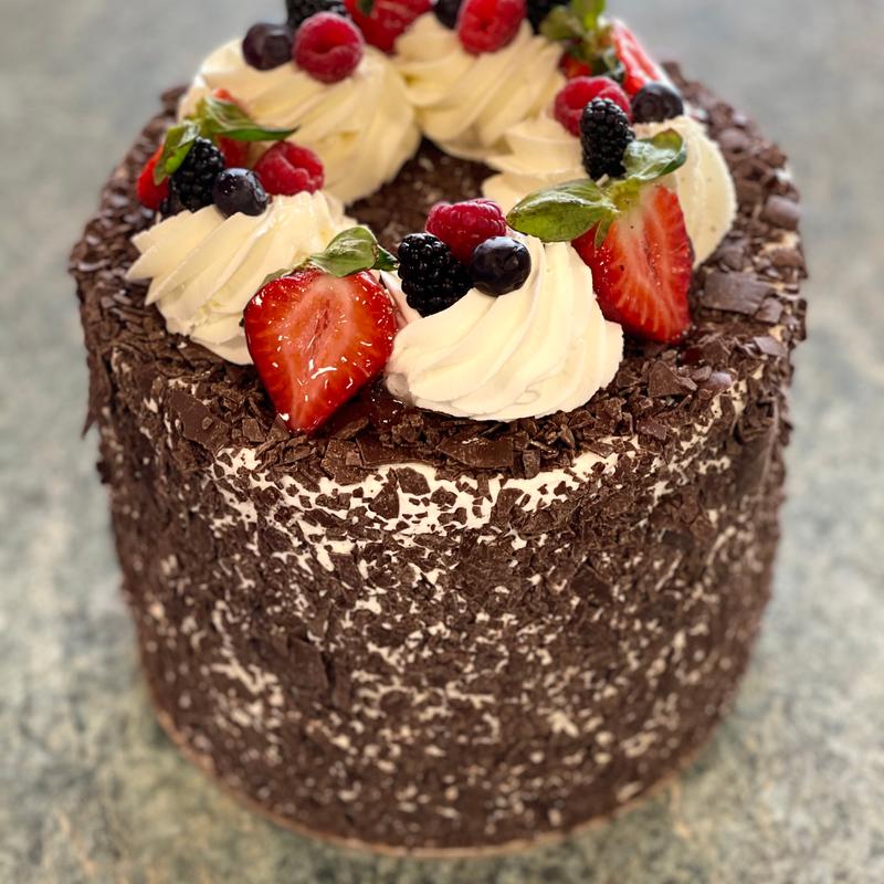 Meli Melo cake with sides pressed in dark chocolate flakes and a ring of piped cream rosettes on top loaded with strawberries, raspberries, blackberries and blueberries.