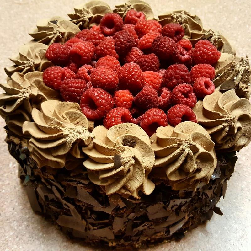 Raspberry truffle cake with chocolate flake sides and a border of piped mocha cream dusted with cocoa, the centre packed with fresh raspberries.