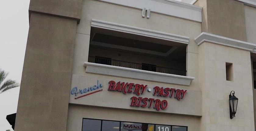 The storefront on West Charleston Boulevard: a two-storey stucco building with a red sign reading French Bakery &middot; Pastry &middot; Bistro above the glass shopfront of suite 110, an iron carriage lantern on the wall to the right and a palm frond at the edge of the frame.